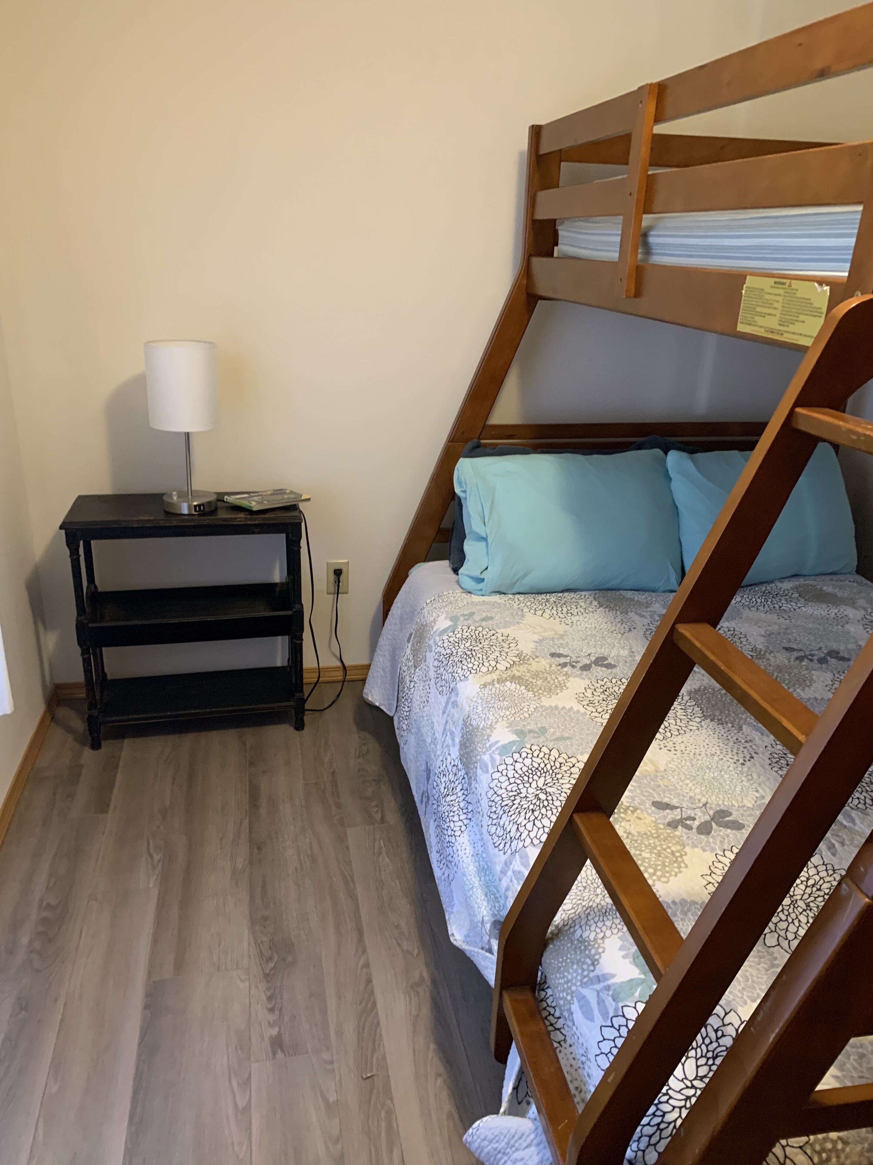 Un lit superposé avec une couvre-lit à motifs, une table de chevet avec une lampe et une prise électrique au mur.