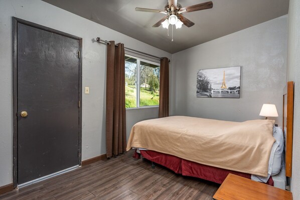 A bedroom with a bed, a ceiling fan, a window with curtains, a door, and a painting of the Eiffel Tower. - NEWLY RENOVATED 2bedroom in heart of Oakhurst (Oakhurst)