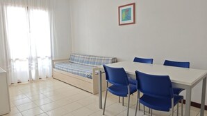 A room with a bed, a dining table with chairs, a small sofa, and a framed picture on the wall.