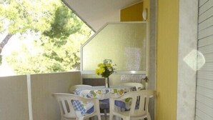 A small outdoor balcony with a table and chairs, a window with a view of trees, and a tiled floor.