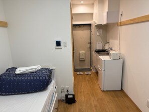 Une chambre d’hôtel compacte comprenant un lit, une petite kitchenette, une douche et un plancher en bois.