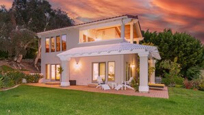 Una casa de dos pisos con un patio cubierto, ventanas amplias y un césped bien cuidado.