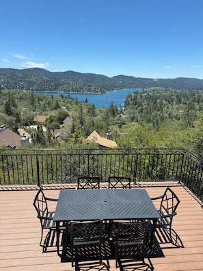 A deck with a table and chairs, overlooking a lake and forested hills.