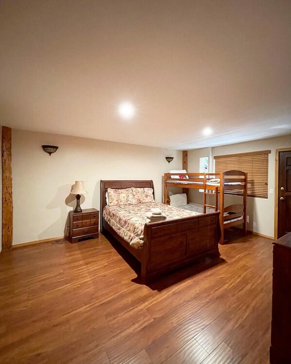 Un dormitorio con una cama de madera, una mesita de noche, una lámpara, una ventana con persianas y una puerta.