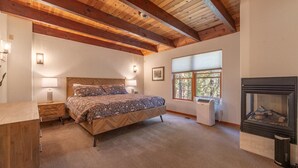 A bedroom with a bed, bedside lamps, a fireplace, and a window with a view of trees. - Amazing 7 Br/ 5.5 Ba Home in Northstar Resort (Truckee)