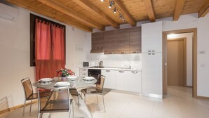 A modern kitchen with white cabinets, a wooden ceiling, and a dining area with a glass table and chairs. - Accogliente alloggio vicino al centro (Verona)