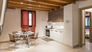 A modern kitchen with white cabinets, a glass dining table, and a red curtain. - Accogliente alloggio vicino al centro (Verona)
