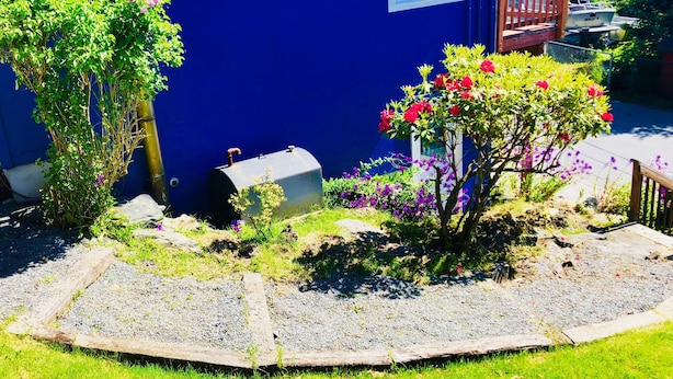Una casa azul con jardín, una terraza de madera y un bote amarrado afuera.