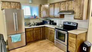 Cocina con armarios de madera, electrodomésticos de acero inoxidable y una ventana con persianas.