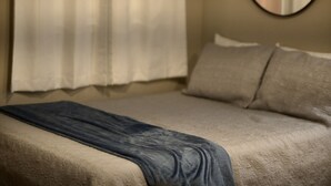 Una cama con una colcha texturizada, un almohadón y un espejo montado en la pared.