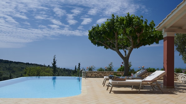 Una piscina con sillas de descanso, un muro de piedra y un árbol.