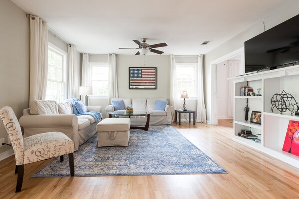 Relax in this stylish living room with a large flat-screen TV, comfortable seating area, and ceiling fan for a cozy atmosphere.