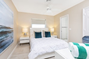 A bedroom with a bed, two bedside lamps, a ceiling fan, a large window, and a door.