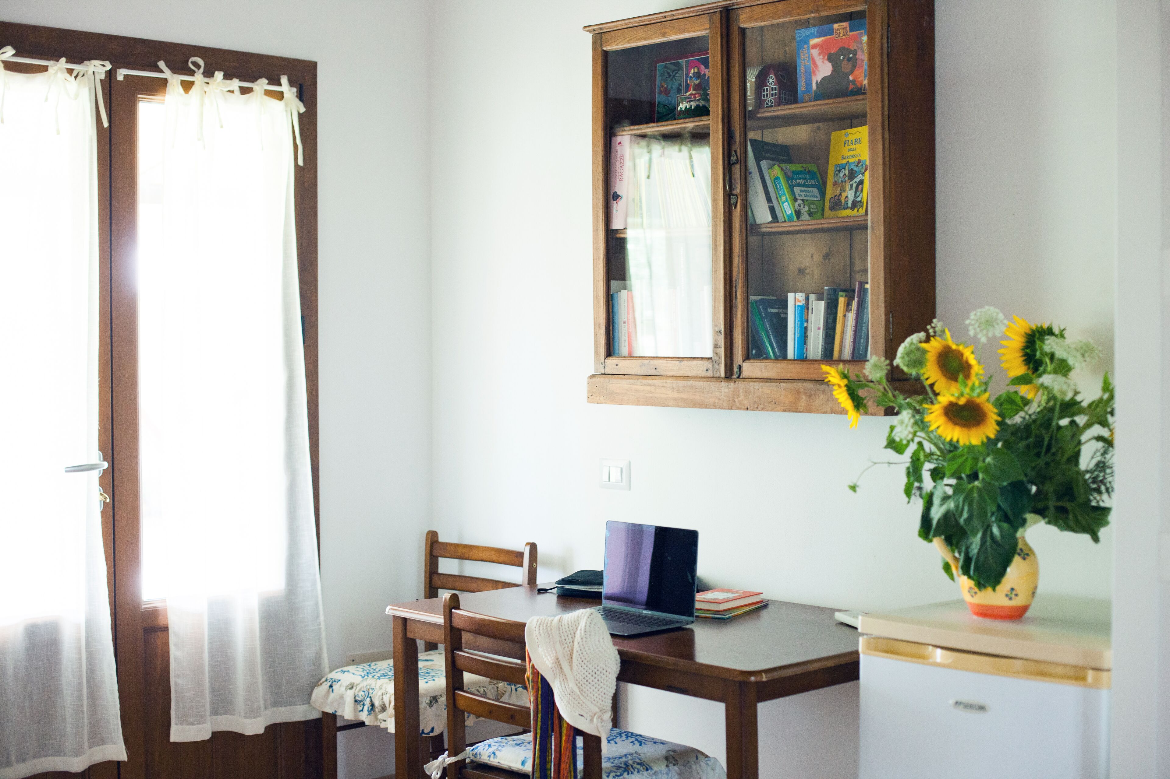 Una stanza con una scrivania in legno, un portatile, una libreria e un vaso con girasoli.