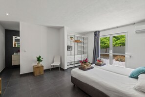 Quarto moderno com cama grande, escrivaninha, guarda-roupa e vista para o verde através de uma janela.