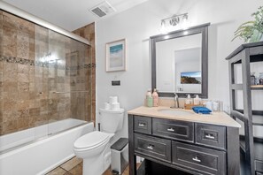 A modern bathroom with a glass-enclosed shower, a white toilet, a sink with a mirror, and a dark vanity with drawers.