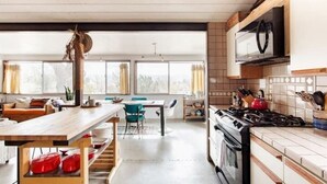 A modern kitchen with a wooden table, a stove, and a dining area with chairs and a sofa. - Diamond Sky Retreat • Joshua Tree, California (Joshua Tree)