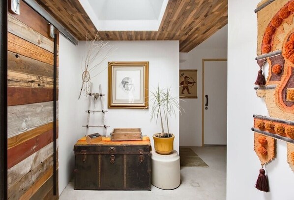 Una habitación con pared de madera, un cuadro enmarco, una planta en maceta y una maleta.