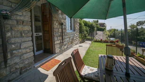 En bygning i sten med en patio, herunder et bord og stole under en grøn parasol.