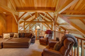A spacious loft with high ceilings, exposed wooden beams, a stone fireplace, and a cozy seating area with leather sofas and armchairs. - Snowgrass Lodge - A River & Mountain Retreat (Leavenworth)
