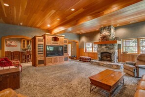 A spacious living room with a stone fireplace, wooden entertainment center, and a cozy seating area. - Snowgrass Lodge - A River & Mountain Retreat (Leavenworth)
