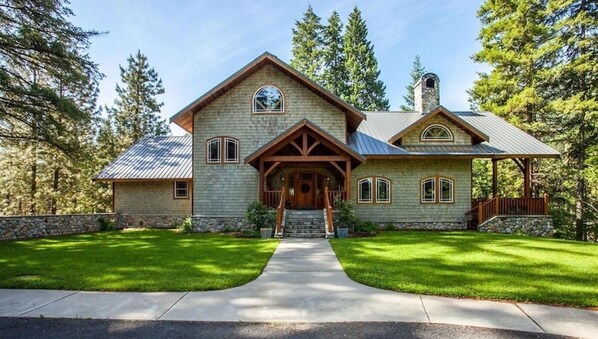 A two-story stone house with a stone chimney, a front porch, and a stone foundation. - Snowgrass Lodge - A River & Mountain Retreat (Leavenworth)