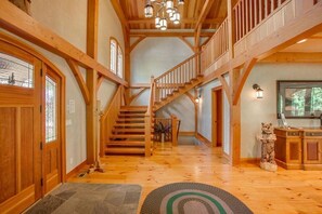 A spacious interior with a wooden staircase, a stone fireplace, and a large window. - Snowgrass Lodge - A River & Mountain Retreat (Leavenworth)