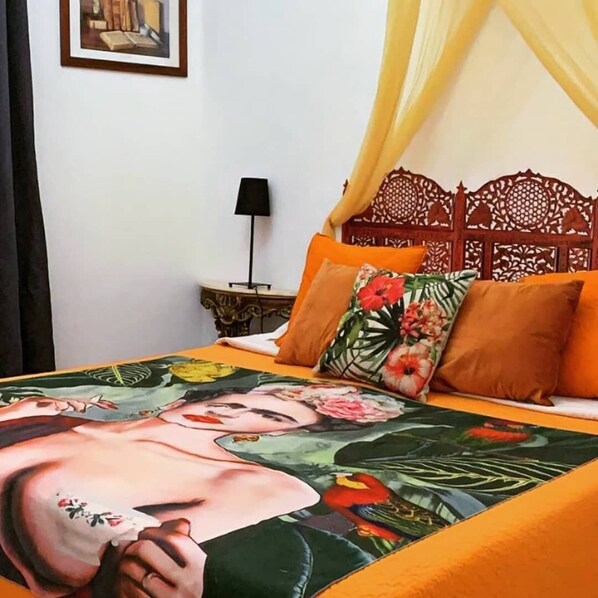 Ein Bett mit floralem Überwurf, einem Holz-Kopfteil und einem orangefarbenen Kissen.