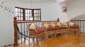 Una escalera con barandilla y balaustradas de madera, que conduce a una habitación con dos sofás de mimbre y cojines estampados, un ventanal con vidrieras y un adhesivo mural de pájaros.