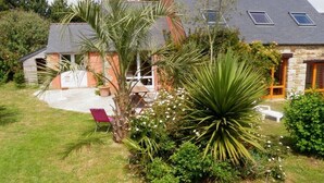 Ein Haus mit Steinverkleidung, einem geneigten Dach und einem kleinen Garten mit einer Palme und Blumen.
