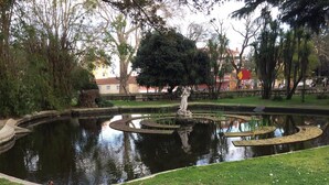 A circular pond with a statue in the center, surrounded by greenery and a fence.