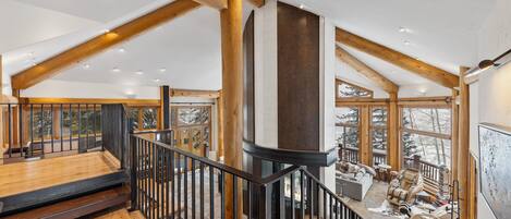 A spacious interior with a high ceiling, wooden beams, and large windows offering views of snow-covered trees.