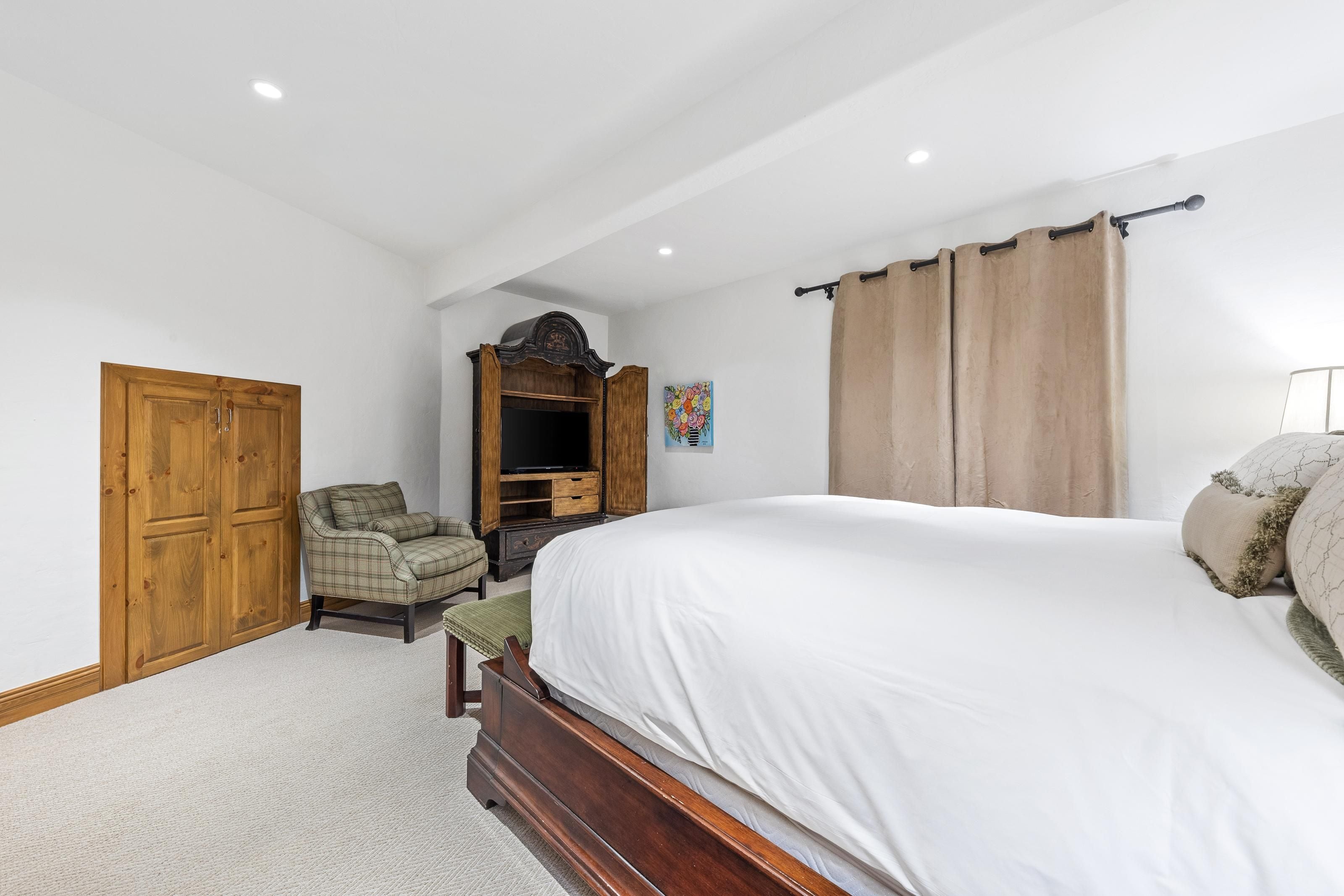 Quarto com cama, guarda-roupa de madeira, cadeira e um armário com televisão.