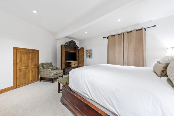 Une chambre à coucher comprenant un lit, une armoire en bois, une chaise et un meuble sur lequel est posée une télévision.