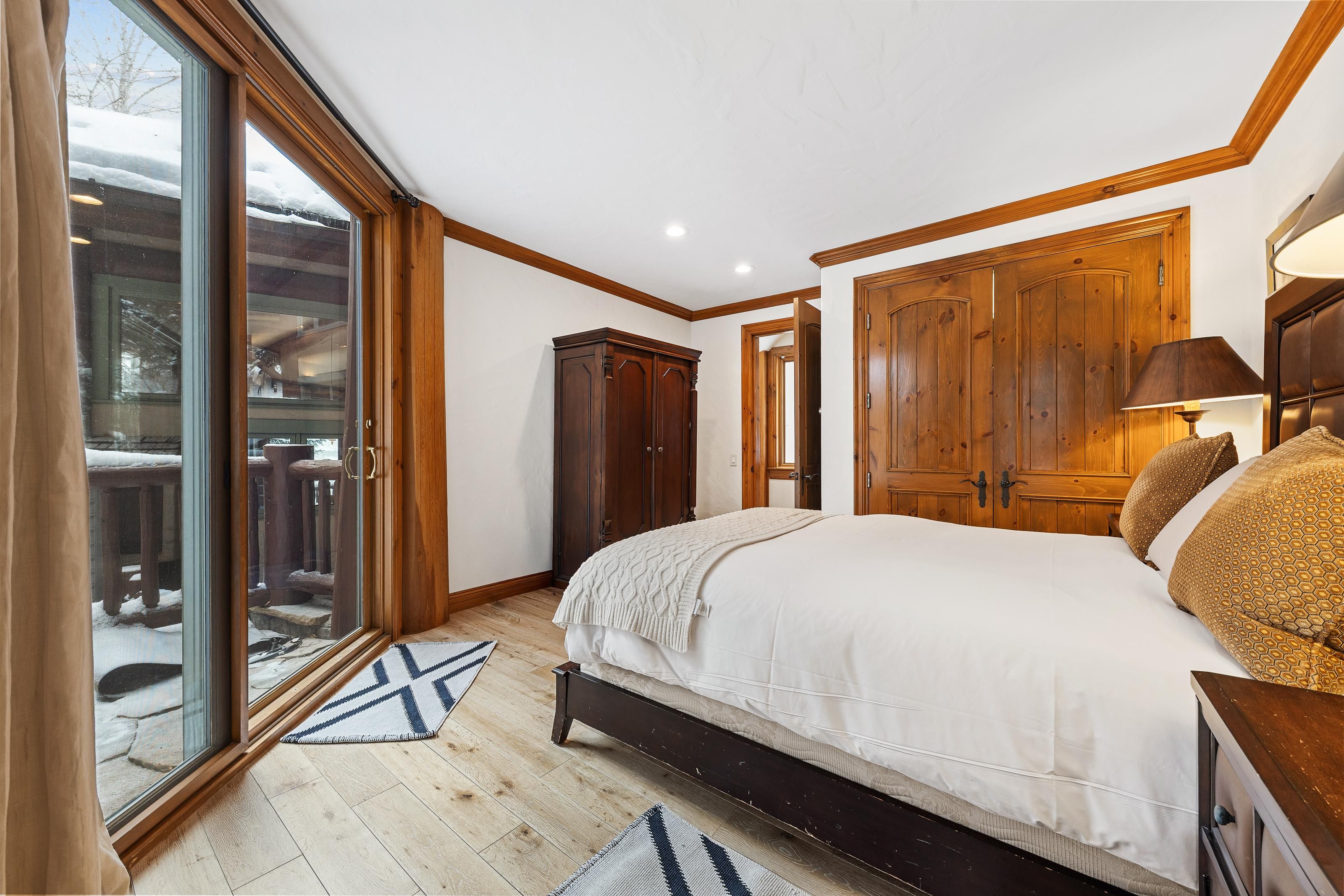 A bedroom with a large bed, wooden wardrobe, and a sliding glass door leading to a balcony.
