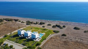 Vue aérienne d’une propriété située sur la côte, avec des bâtiments modernes blancs, une piscine et une plage.