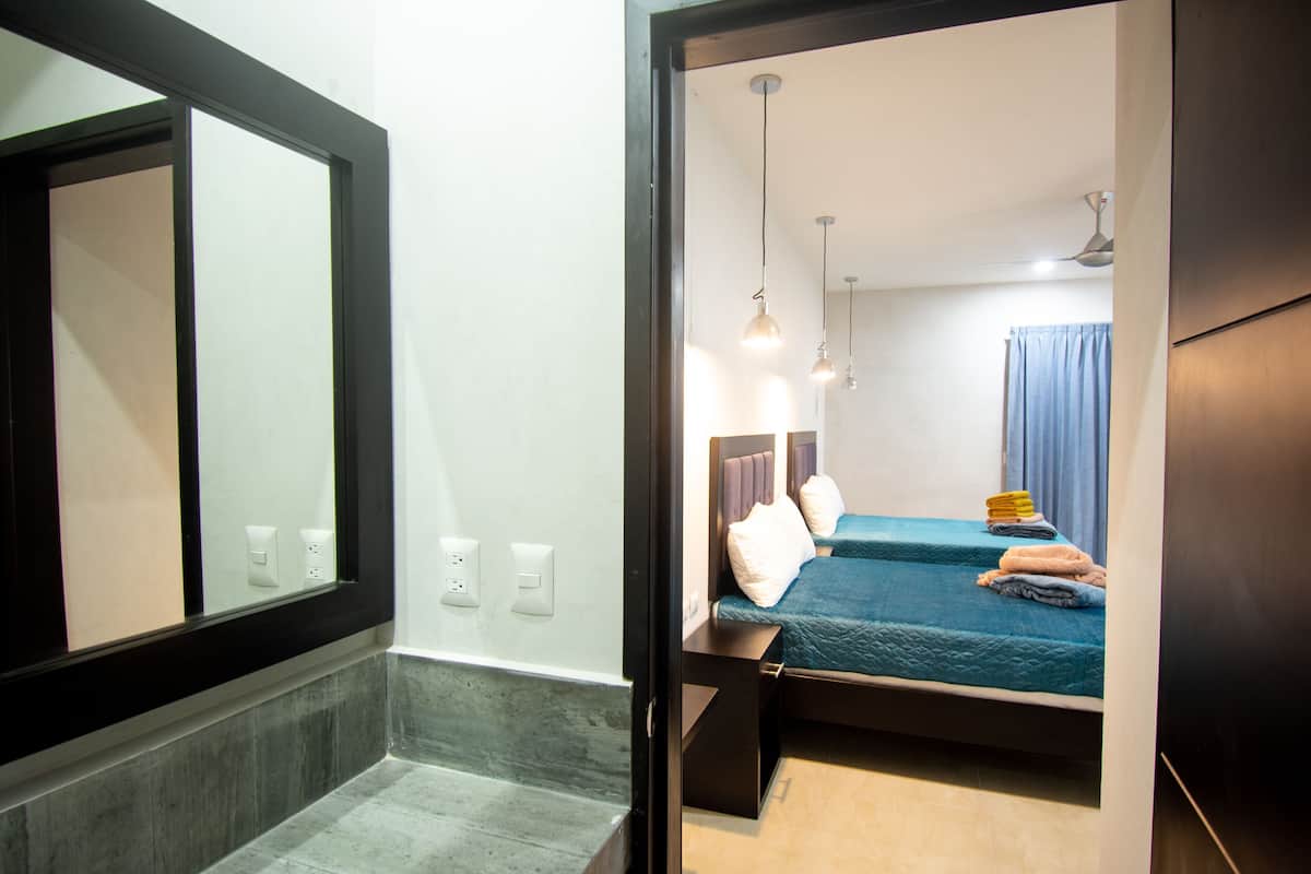 Una habitación de hotel con un espejo grande, una cama con cubrecama azul, una mesita de noche y un ventilador de techo.