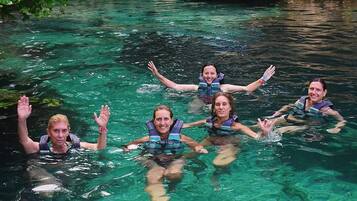 Un grupo de personas nadando en una masa de agua clara y natural rodeada de rocas y vegetación.