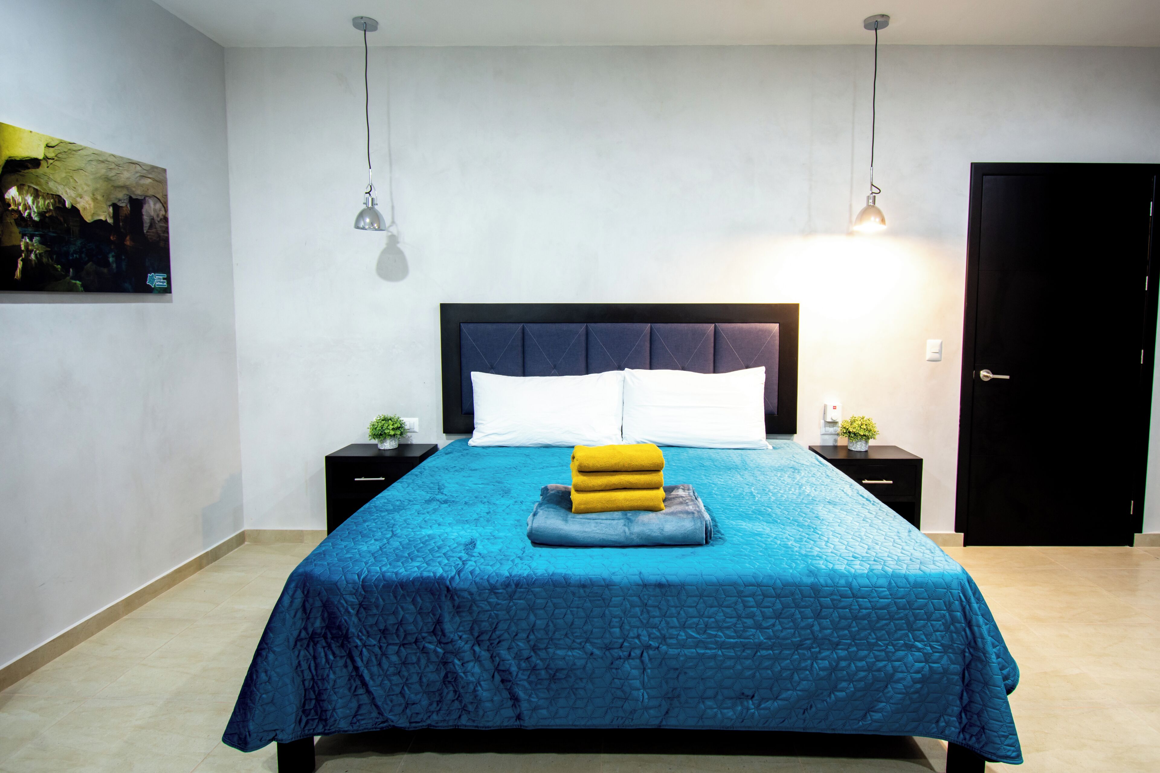Une chambre à coucher comprenant un lit, des tables de chevet, une commode, une porte et une lampe fixée au mur.