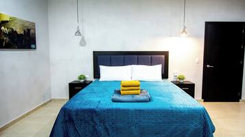 Une chambre à coucher comprenant un lit, des tables de chevet, une commode, une porte et une lampe fixée au mur.