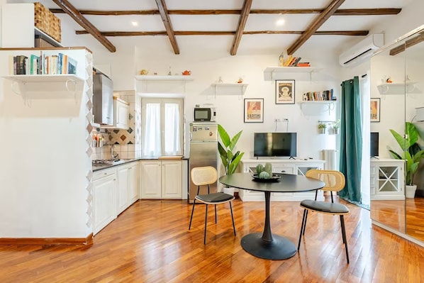 A modern kitchen with white cabinets, a dining area with a round table and chairs, and a TV mounted on the wall.
