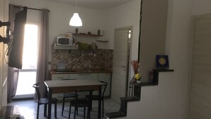 Una pequeña cocina con microondas, pileta y comedor con sillas.