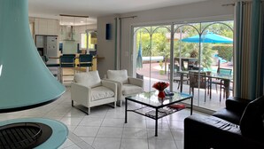 Un salón moderno con una mesa de centro de vidrio, sofás blancos y vistas a un patio exterior con sombrillas.
