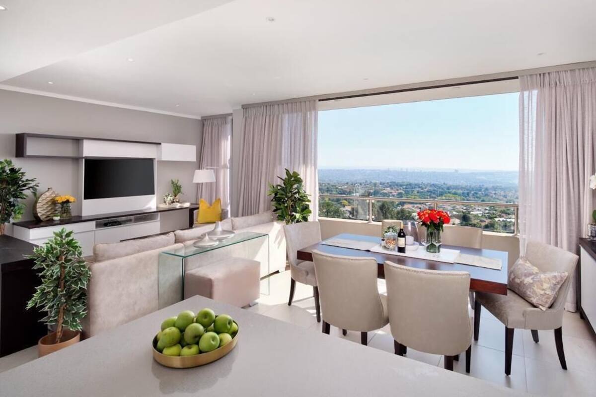 Una sala de estar moderna con televisor de pantalla plana, una mesa de centro de vidrio y un comedor con vista a la ciudad.
