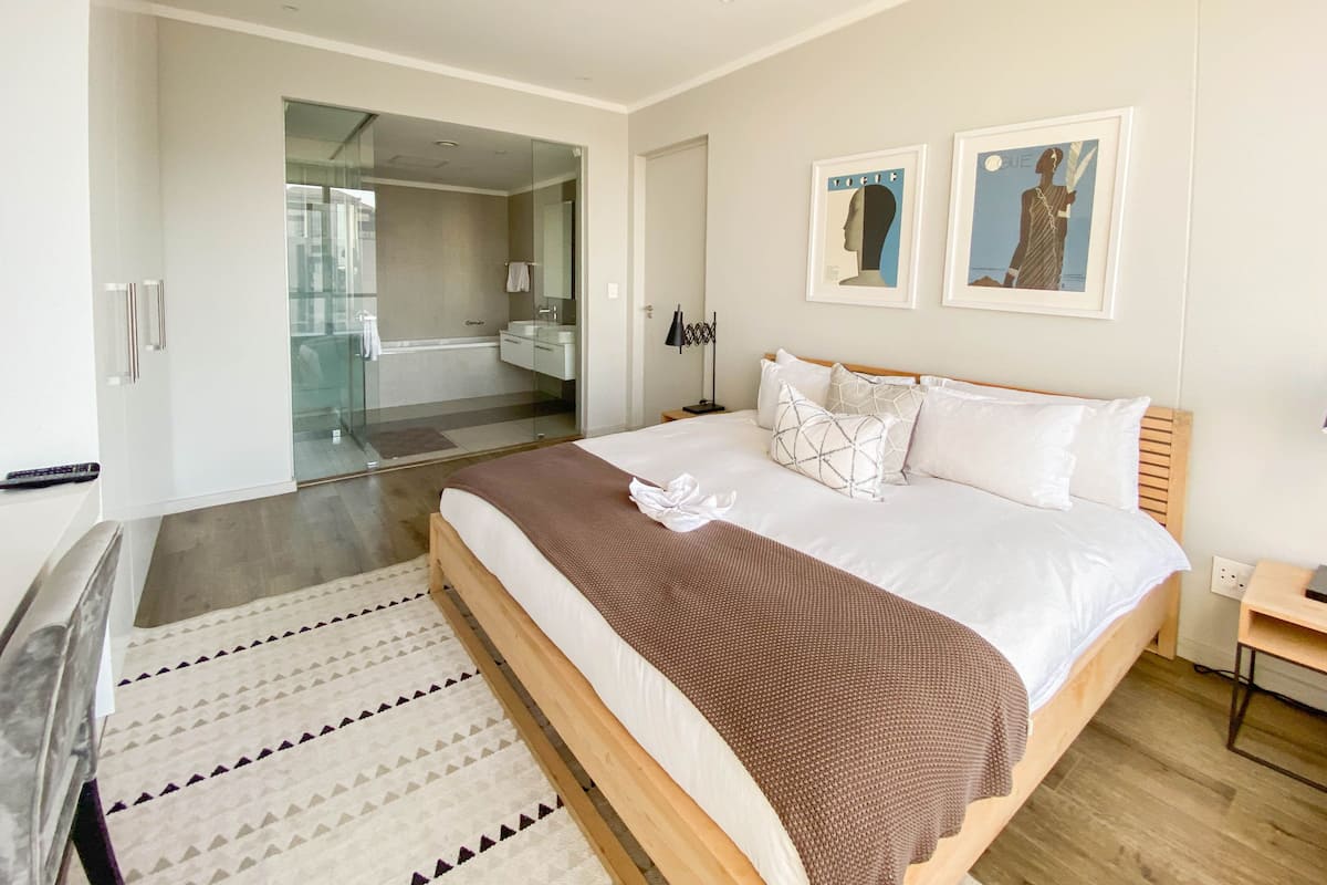 Una habitación de hotel moderna con una cama grande, cabina de ducha de vidrio y vistas a la ciudad.