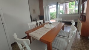 Een eetgedeelte met een houten tafel, witte stoelen en uitzicht op het landschap door grote ramen.