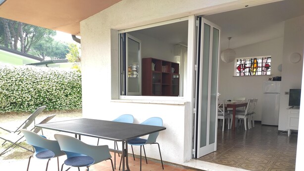 Een open terras met een tafel en stoelen, een schuifdeur naar een keuken en een welkomstmat.