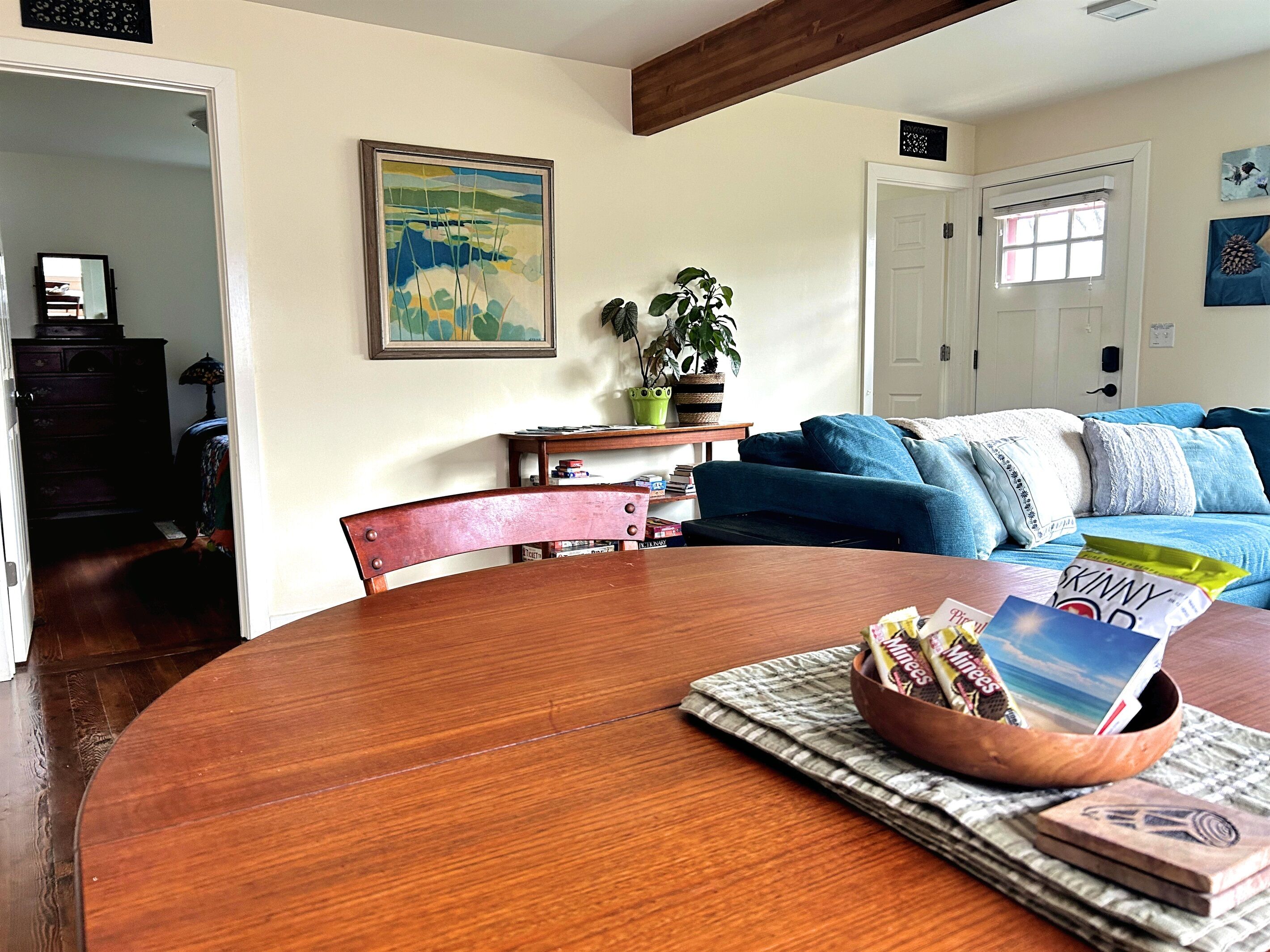 A dining area with a wooden table, a bowl of snacks, and a painting on the wall.