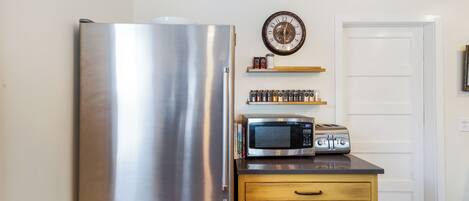 A compact kitchen with a stainless steel refrigerator, a microwave, and a toaster on the counter.