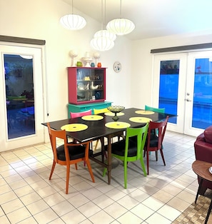 Un coin repas avec une table noire, des chaises colorées et un buffet rouge aux portes en verre.